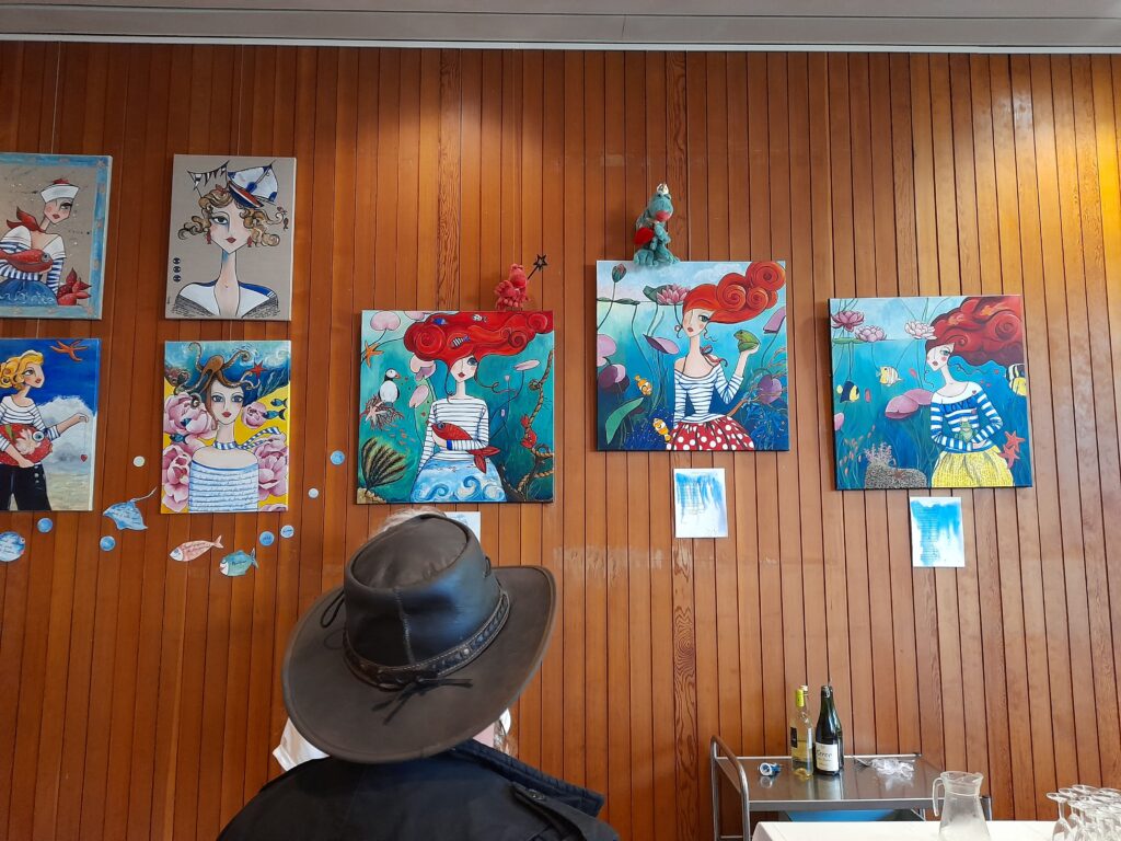 Photo de l'exposition Peintures et poèmes de Manuele Lenoir. Lorsqu'un homme observe les tableaux installées dans le séjour de l'auberge de jeunesse Ostal Brest.